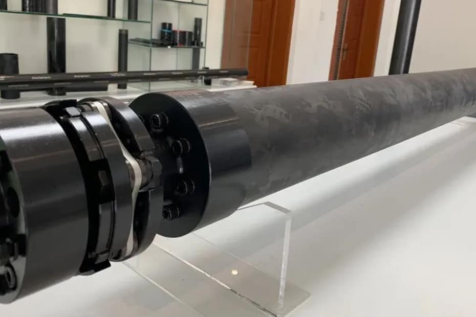 Close-up of a high-torque custom carbon fiber drive shaft featuring precision-bonded metal end fittings for industrial power transmission.