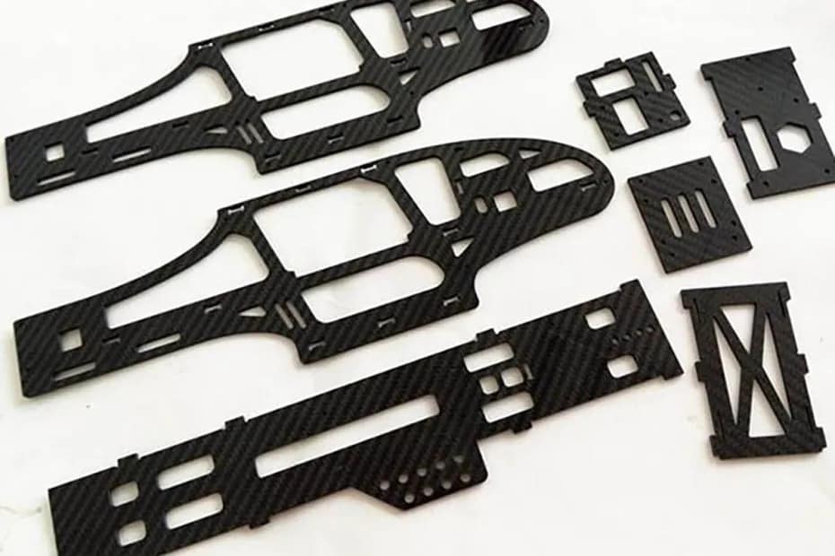 Multiple intricate CNC machined carbon fiber parts with glossy 3K twill finish, including complex cutouts for UAV frames and industrial automation components, showing high-precision edge quality.